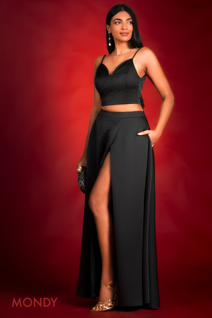 Woman wearing a black Crop top and a maxi skirt with a high slit on a red background